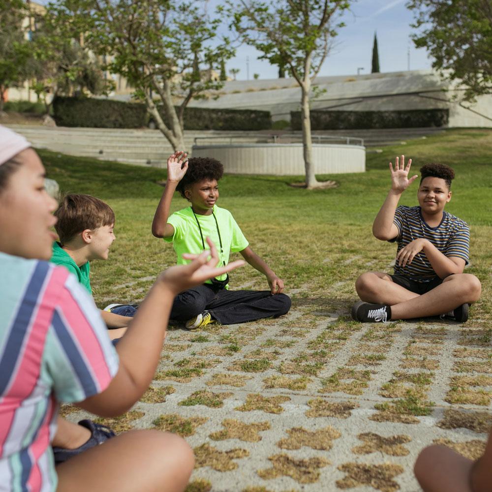 Diverse kids sit in a circle in a grassy park after school playing a game